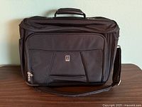 Front view showing Travelpro logo, front organizer pocket, top handle, shoulder strap