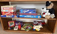 Shelf with board games, plush bears, toys, lunch box, vehicles and books