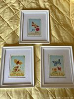 Three matching white-framed prints laid out on quilted surface
