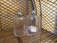 Two clear ribbed glass jars side by side, one containing cotton balls