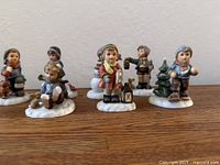 Close view of six Hummel winter child figurines on wood surface
