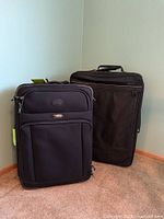 Two black rolling suitcases standing side by side