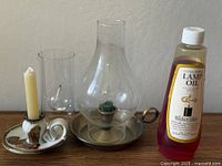 All items together: brass lamp with chimney, spare chimney glass, stoneware candleholder with candle, lamp oil bottle