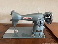 Left profile of White rotary sewing machine mounted in cabinet, showing full body and needle plate