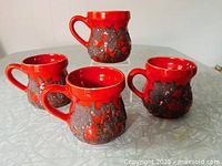 Four red lava drip mugs arranged on table