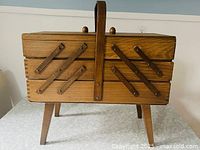 Full front view of closed wooden accordion sewing box on legs