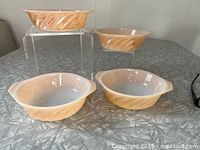 Four Peach Lustre casseroles grouped on table, two elevated on clear riser showing exterior ribbing
