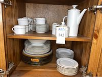 Cabinet view of stacked plates, bowls, chargers, cups, coffee pot, sugar and creamer