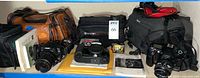 Overall lot showing four camera bodies, three bags, manuals, film and accessories on shelf