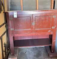 Front view of red painted wood cabinet with two doors and lower shelf