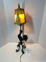 Full view of lamp illuminated showing rooster base, shade, cord
