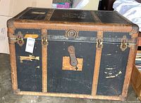 Front view of black vintage steamer trunk showing hardware and wear