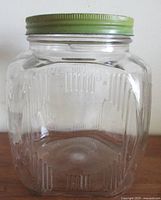 Front view of clear ribbed glass Dominion Hoosier jar with green lid