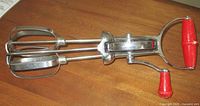 Full view of stainless hand egg beater showing twin beaters and red handle