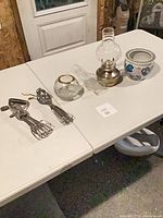 All items on table: planter, oil lamp, spare chimney, glass bowl, two egg beaters