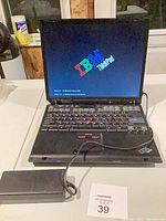 Front view of IBM ThinkPad laptop open, screen on with logo, power adapter connected