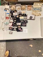 Overall view of entire lot laid out on table with multiple boxes and loose jewelry pieces