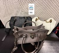 Front view of all three handbags: black Calvin Klein crossbody, grey Michael Kors Hamilton tote, white Michael Kors Lilly bag