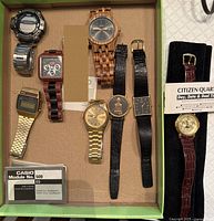 Tray showing eight assorted wristwatches including wood, digital, analogue and Citizen watch on stand, plus Casio booklet