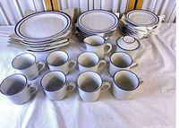 Full dinnerware set laid out: stack of large, medium, small plates, row of mugs, creamer and sugar bowl