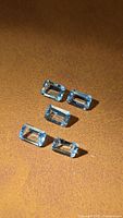 Five emerald-cut aquamarine stones on brown background, showing size and colour