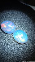 Pair of oval cabochon opals on black background showing play of colour