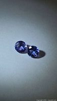 Pair of round bluish-violet faceted gemstones on neutral background
