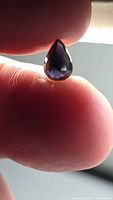 Pear-cut purple spinel held between fingers, front view