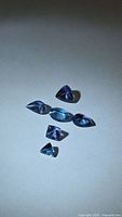 Six loose violet-blue tanzanite gemstones arranged on white background