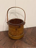 Front view of antique wooden bucket showing staves, metal bands, bentwood handle upright