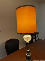 Full view of one lamp illuminated showing amber shade, glass midsection, and metal base