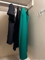 Three garments hanging: navy jacket, navy skirt, green piece