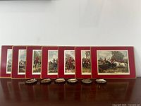 Front view of 8 placemats with red borders and 6 coasters displaying fox-hunting scenes