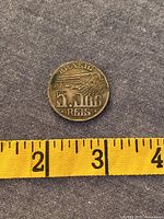 Reverse of coin with denomination, date and wing motif against measuring tape for scale