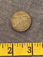 Reverse of 1936 5.000 Réis coin with wing design and tape measure for scale