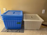 Stacked blue and white wheeled storage bins with lids nearby