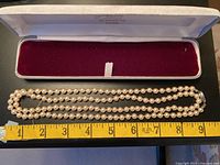 Two-strand pearl necklace laid beside ruler in open case