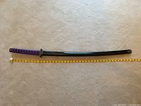 Full view sword in scabbard next to tape measure