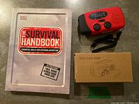 Lot overview showing Survival Handbook book, red solar crank radio, and radio box