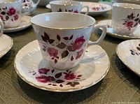 Cup and saucer showing rose pattern with gold rim; additional cups and saucers in background