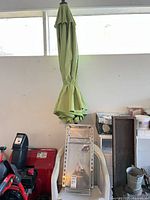 Closed green umbrella resting against beige plastic chair