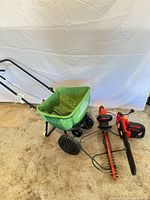Overview of broadcast spreader with two red corded tools on floor