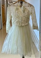 Full view of lace dress with tulle skirt and matching bolero jacket on hanger