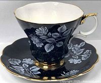 Teacup on saucer showing floral decor, gold trim, white interior