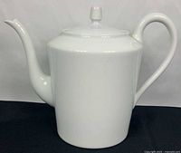 Front view of white porcelain Limoges teapot with lid, showing spout and handle