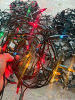 hand holding multicolour mini light string illuminated, other coils in background