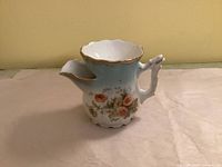 side view of porcelain shaving scuttle showing floral design, handle and spout