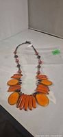 Full view of necklace showing orange oval and bar beads with brown spacers on dark cord