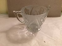 Oblique view of clear pressed-glass creamer showing iris pattern and handle