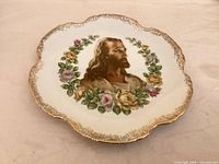 Front view of porcelain plate showing Jesus portrait, floral wreath, scalloped gilt rim